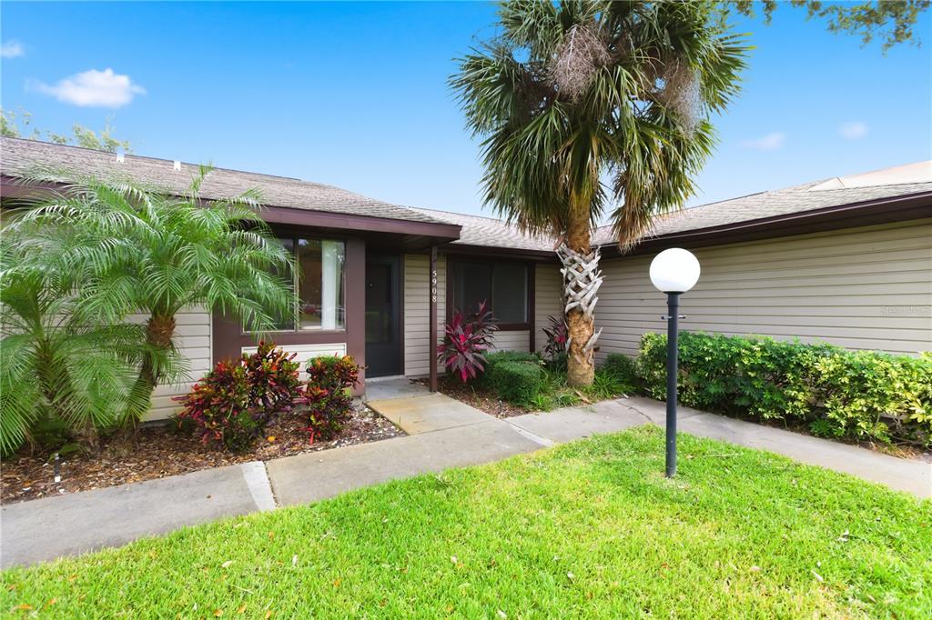 A single-story house exterior features beige horizontal siding, a brown front door, and landscaping — 5908 36TH AVENUE CIRCLE W, BRADENTON, FL
