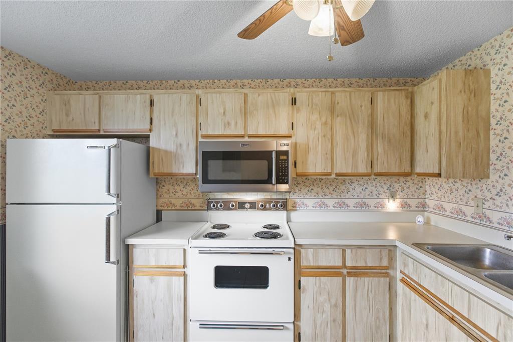 A kitchen features light wood cabinets, white appliances, and floral wallpaper above the countertops — 5908 36TH AVENUE CIRCLE W, BRADENTON, FL