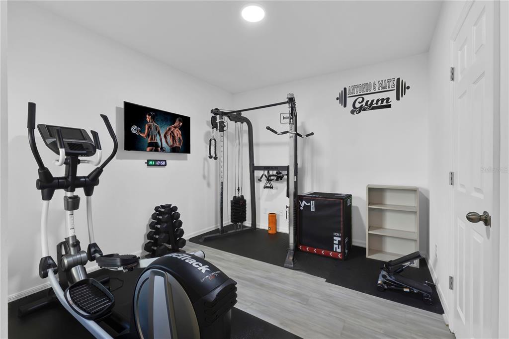 A home gym features an elliptical machine, a cable weight station, dumbbells, and a plyometric box — 5018 ROYAL POINT AVENUE, KISSIMMEE, FL