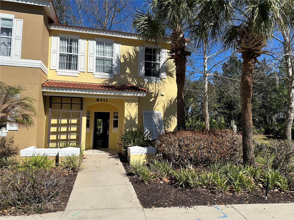 A two-story yellow stucco building features a tiled roof, a front walkway, and palm trees — 8411 CRYSTAL COVE LOOP, KISSIMMEE, FL