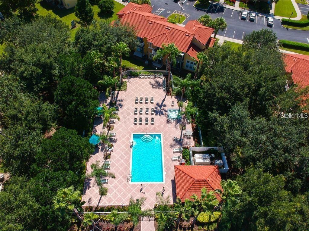An aerial view shows a rectangular swimming pool surrounded by a patio, palm trees, and buildings — 8411 CRYSTAL COVE LOOP, KISSIMMEE, FL