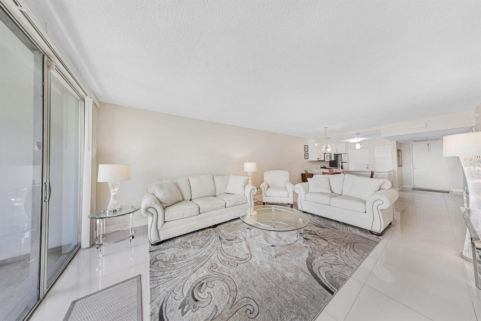 A living room with white sofas, a glass coffee table, and a patterned area rug — 3091 N Course Drive # 102, Pompano Beach FL 33069, POMPANO BEACH, FL
