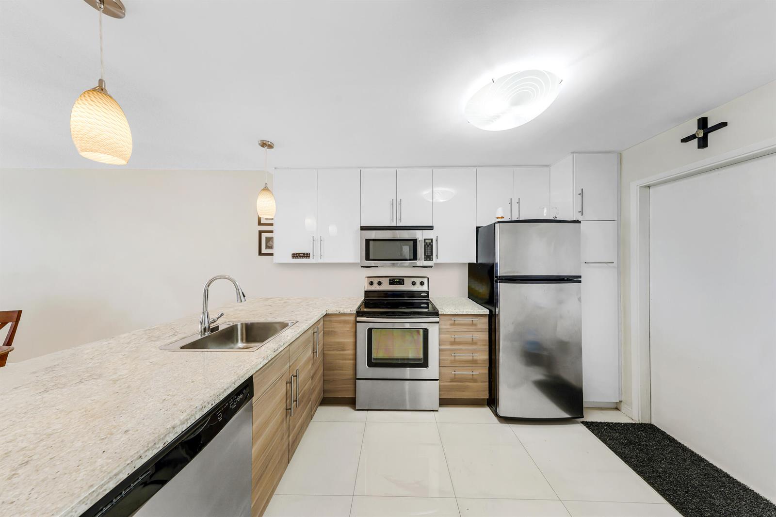 A kitchen features white upper cabinets, wood-tone lower cabinets, stainless steel appliances, and granite countertops — 3091 N Course Drive # 102, Pompano Beach FL 33069, POMPANO BEACH, FL