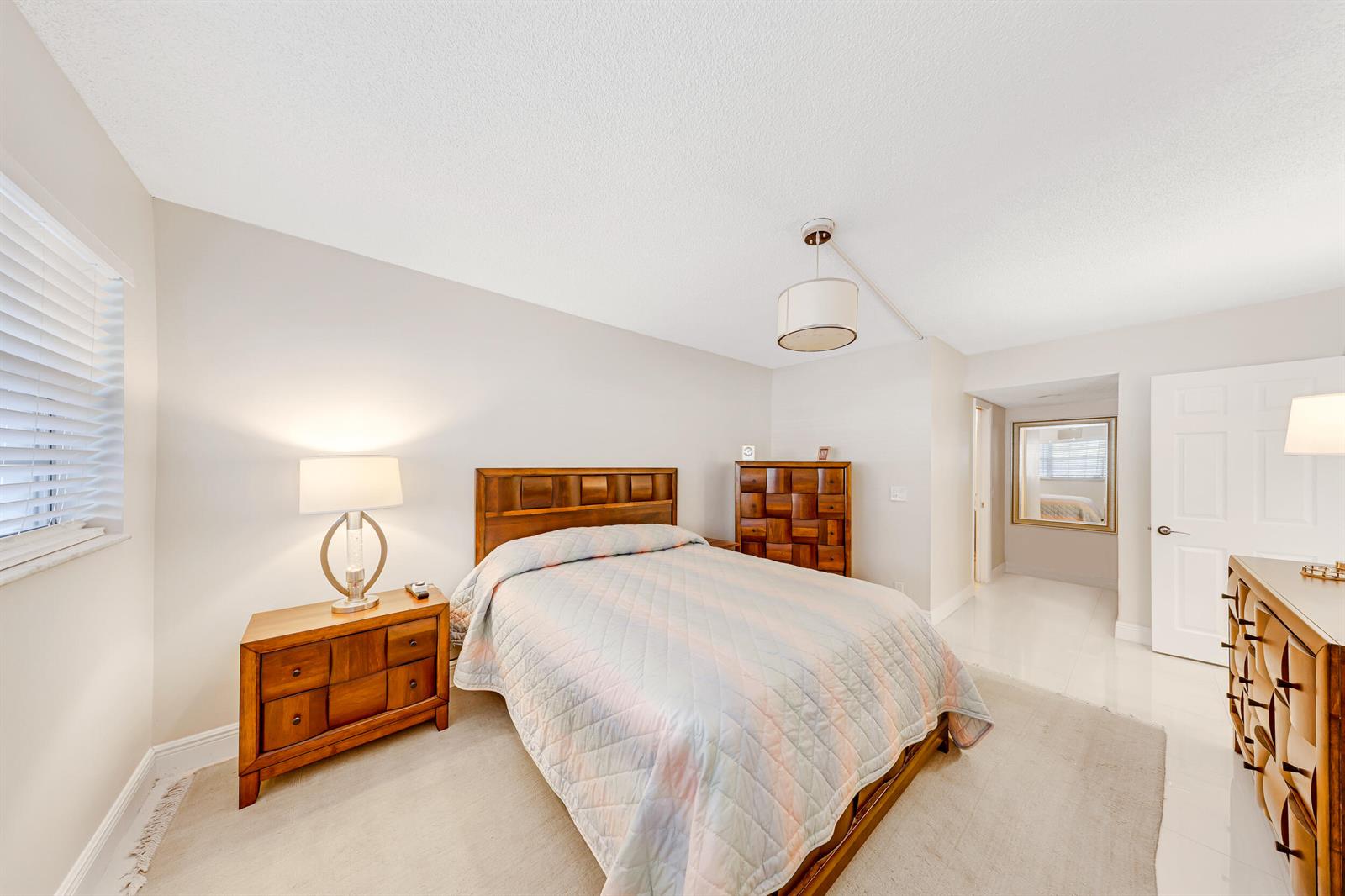 A bedroom features a wooden bed frame, matching nightstand and dresser, and a light-colored quilt — 3091 N Course Drive # 102, Pompano Beach FL 33069, POMPANO BEACH, FL