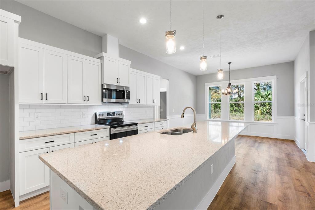 A kitchen features white cabinets, a large quartz island, stainless appliances, and wood-look flooring — 0 SW KIMBERLY LANE LOT 6 DRIVE, LAKE CITY, FL
