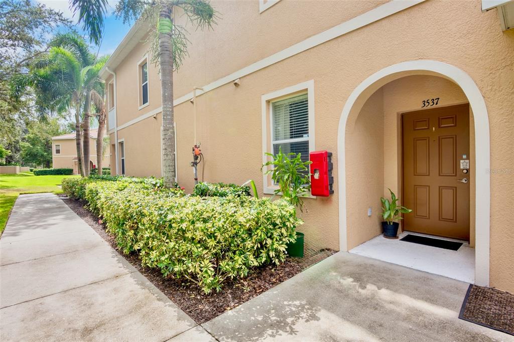 An exterior view of a tan stucco building with a brown front door and landscaping — 3537 PARKRIDGE CIRCLE UNIT 15-106, SARASOTA, FL