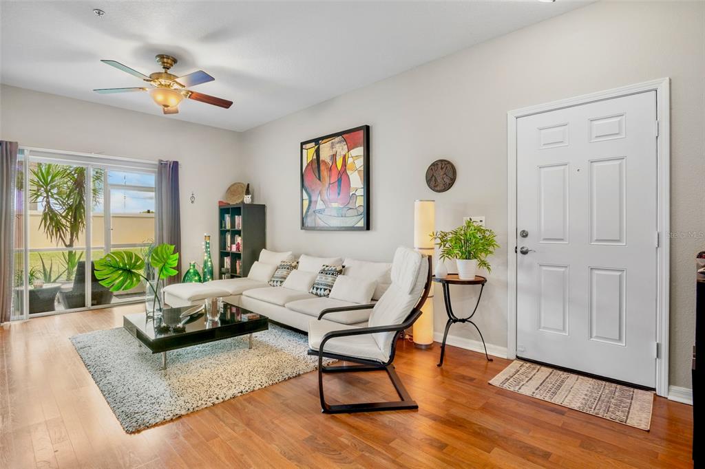 A living room features a white sectional sofa, a glass coffee table, and wood flooring — 3537 PARKRIDGE CIRCLE UNIT 15-106, SARASOTA, FL