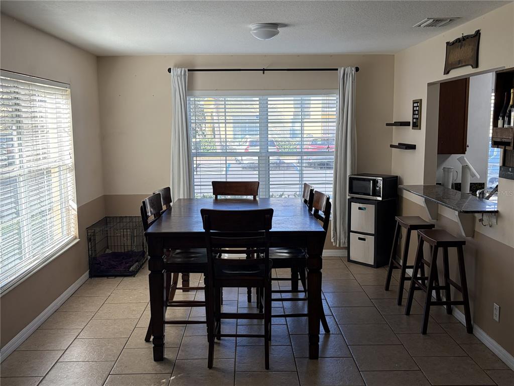 A dining area features a dark wood table with chairs, tile flooring, and a breakfast bar — 3858 ISLAND WAY, ST PETERSBURG, FL