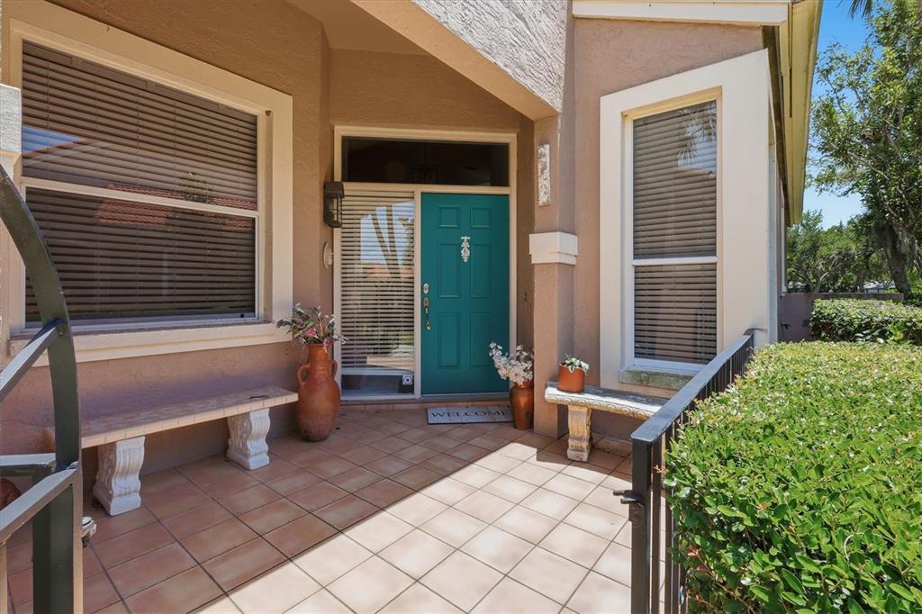 A tiled front porch features a teal door, two stone benches, and potted plants — 4636 DEER TRAIL BOULEVARD, SARASOTA, FL
