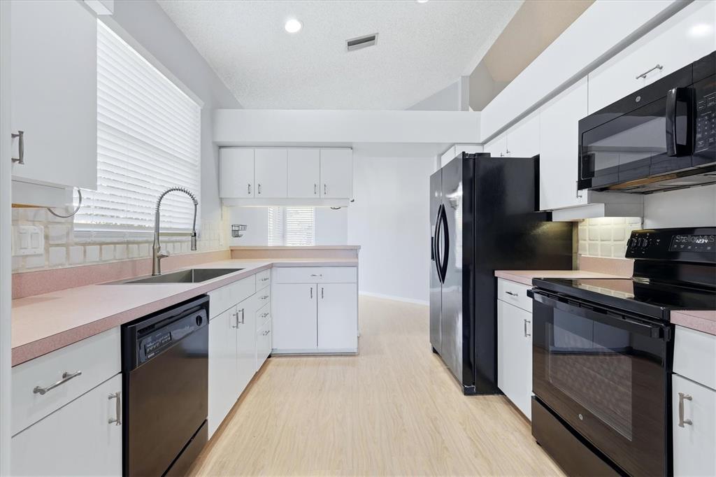A kitchen with white cabinets, pink countertops, black appliances, and light-colored wood-look flooring — 4636 DEER TRAIL BOULEVARD, SARASOTA, FL