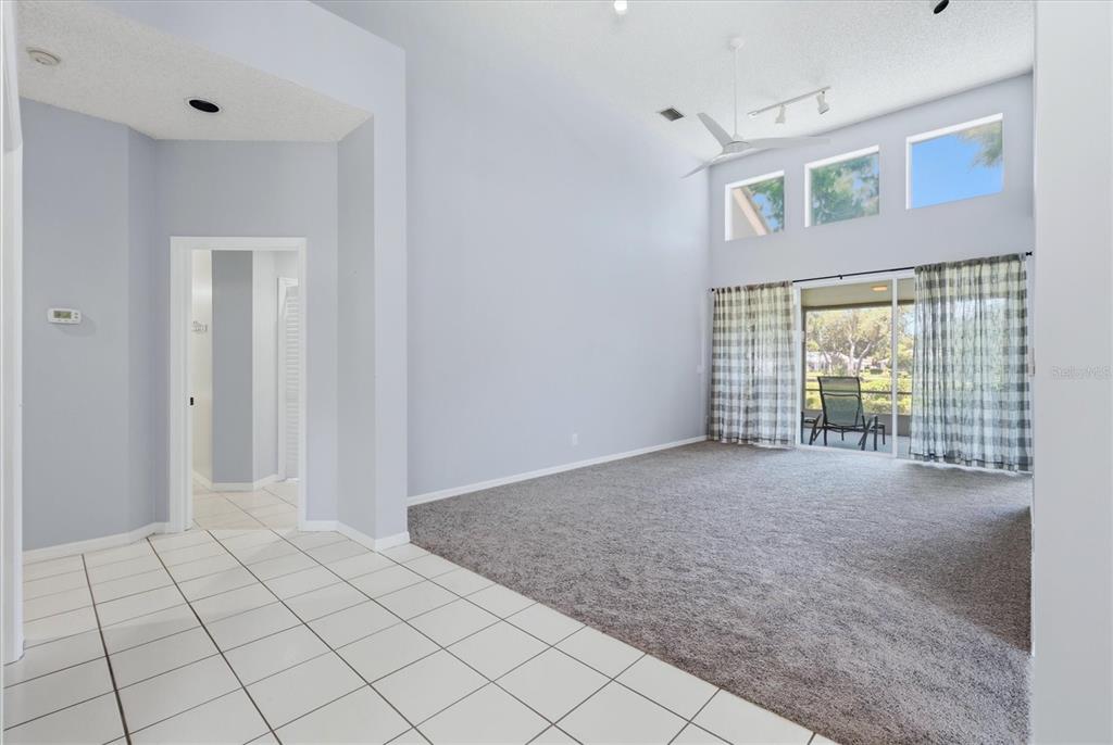 A living room with vaulted ceilings, gray carpet, and a sliding glass door to a patio — 4636 DEER TRAIL BOULEVARD, SARASOTA, FL