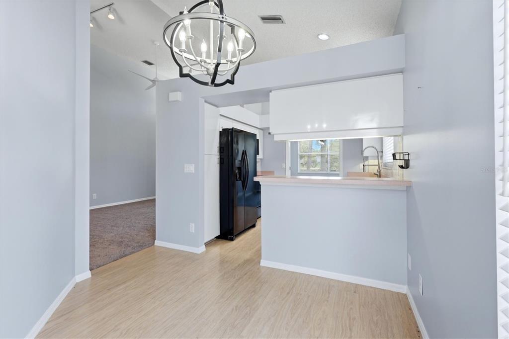 A dining area with light wood flooring leads to a kitchen featuring a black refrigerator — 4636 DEER TRAIL BOULEVARD, SARASOTA, FL