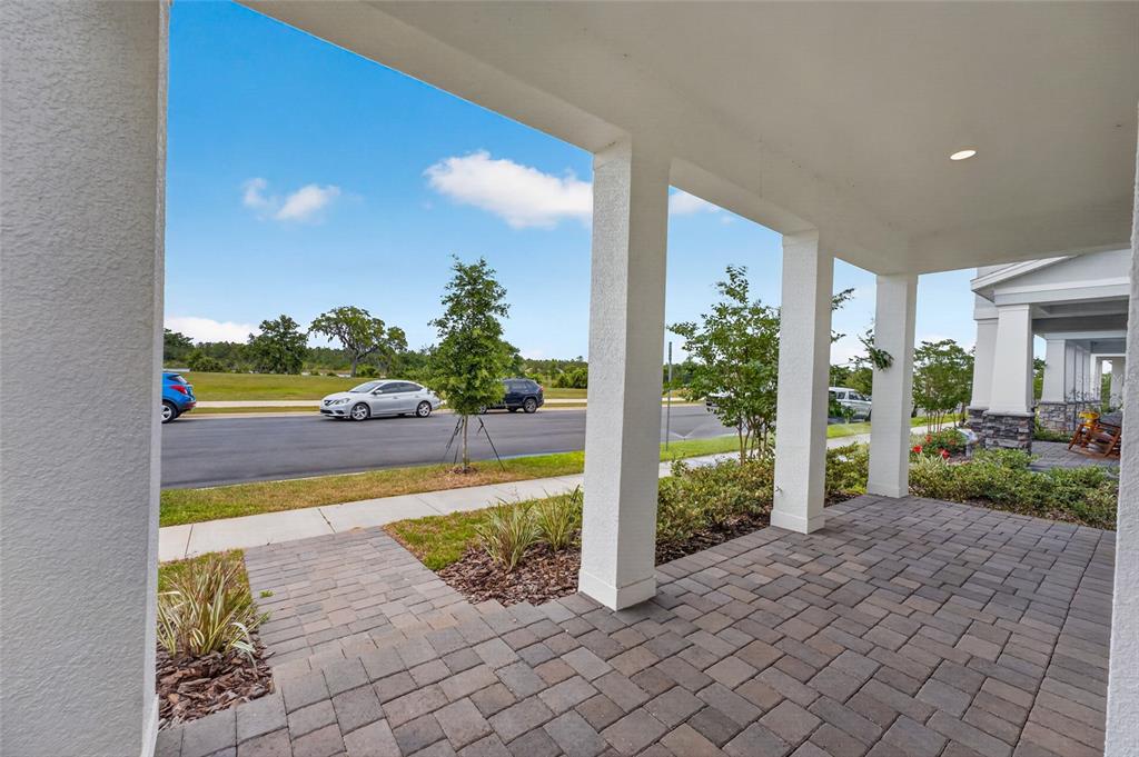 A covered front porch with paver flooring overlooks a street with parked cars and landscaping — 15174 FIELD DAISY DRIVE, WINTER GARDEN, FL