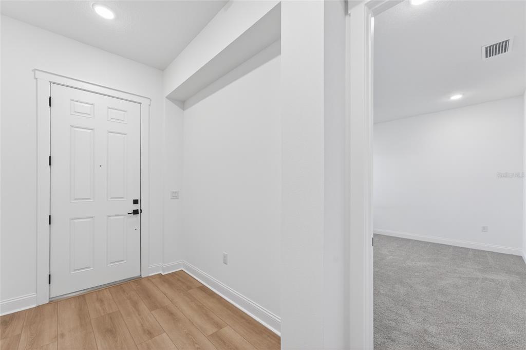 An entryway with wood-look flooring leads to a carpeted room through an open doorway — 15174 FIELD DAISY DRIVE, WINTER GARDEN, FL