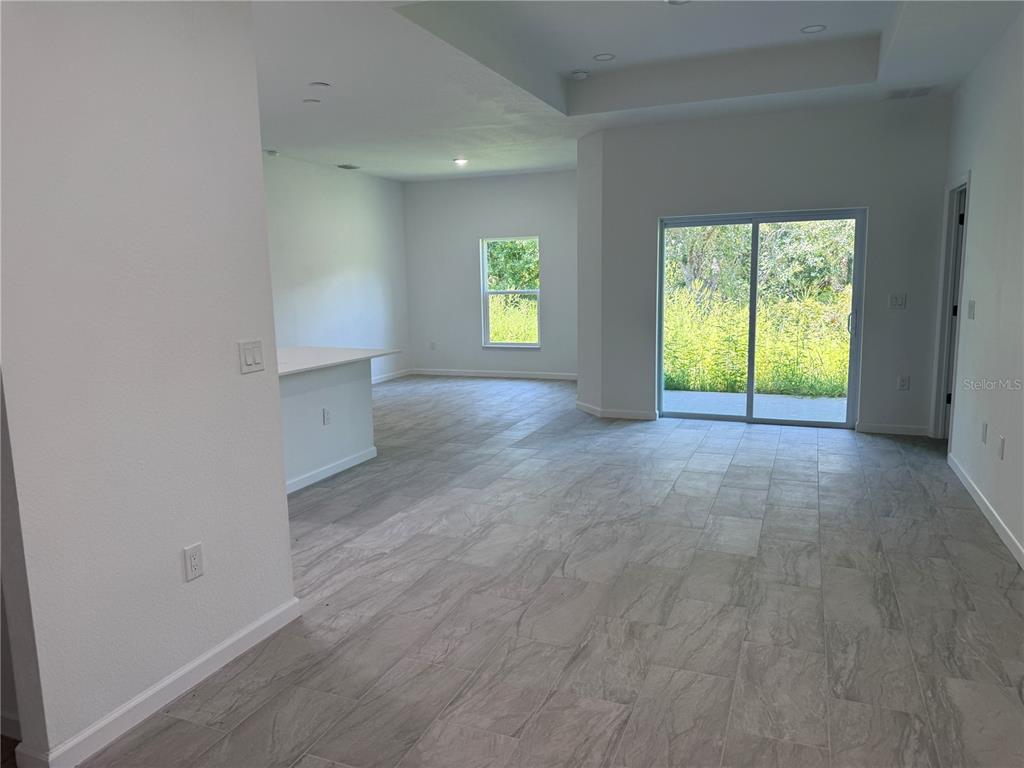 An open-concept living area features light gray tile flooring, white walls, and a sliding glass door — 2669 MAXIMO ROAD, NORTH PORT, FL