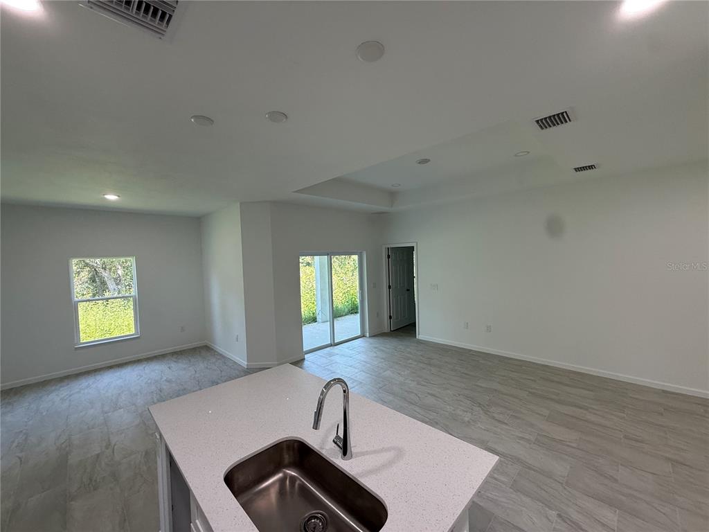 A kitchen island with a stainless steel sink sits in an open-concept room with tile floors — 2669 MAXIMO ROAD, NORTH PORT, FL
