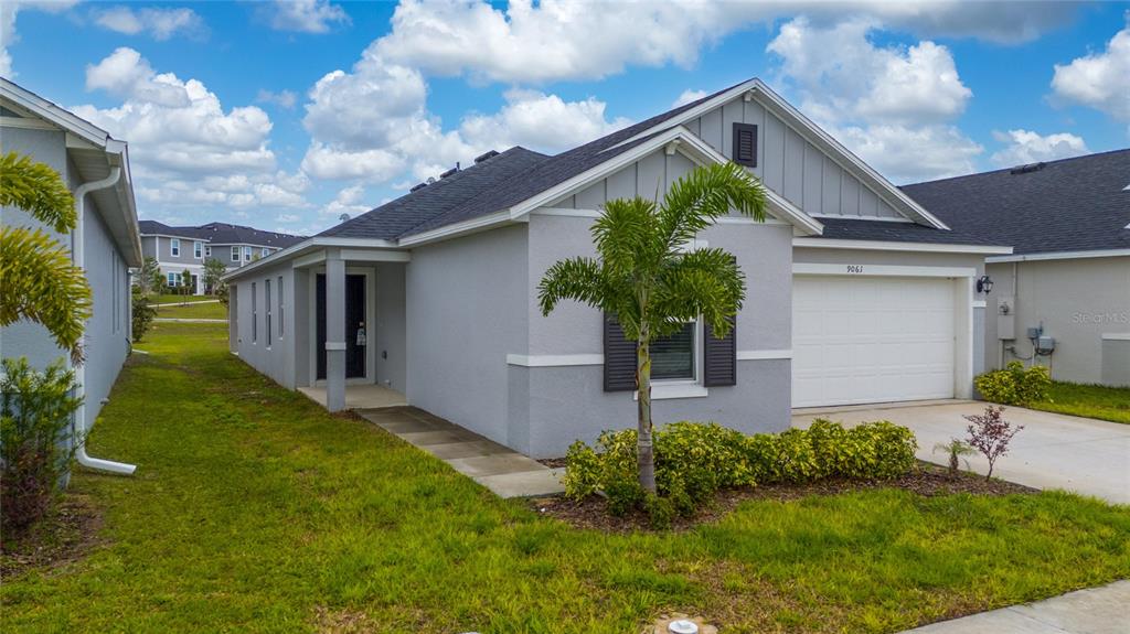 A single-story gray house with a white garage door, a palm tree, and a lawn — 9061 OSCRAFT DRIVE, DAVENPORT, FL