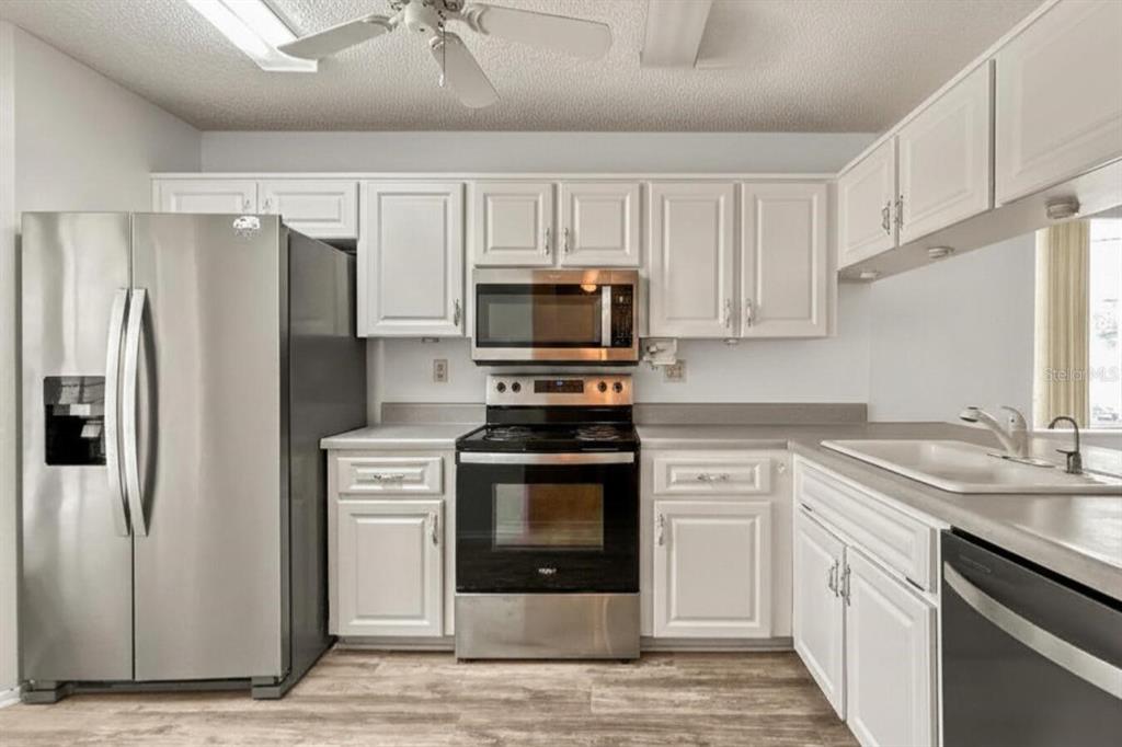 A kitchen with white cabinets, stainless steel appliances, and light wood-look flooring — 6419 REMUS DRIVE, NEW PORT RICHEY, FL