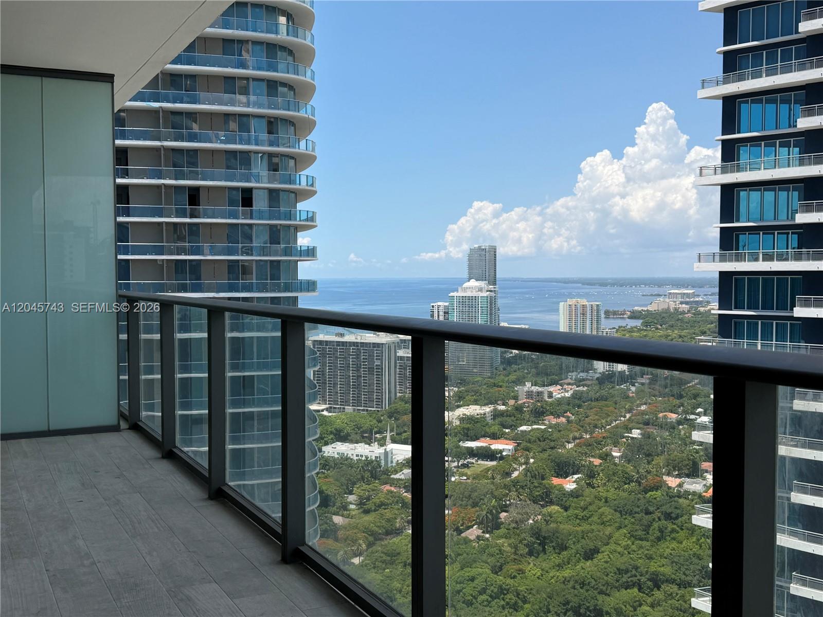 A high-rise balcony with a glass railing overlooks a city skyline and the ocean — 1300 S Miami Ave # 4108, Miami FL 33130, MIAMI, FL