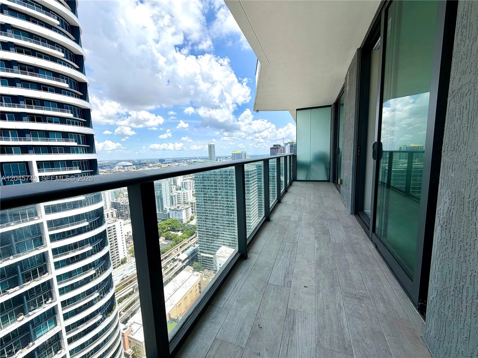 A high-rise balcony features gray wood-look tile flooring and a glass railing overlooking a city — 1300 S Miami Ave # 4108, Miami FL 33130, MIAMI, FL