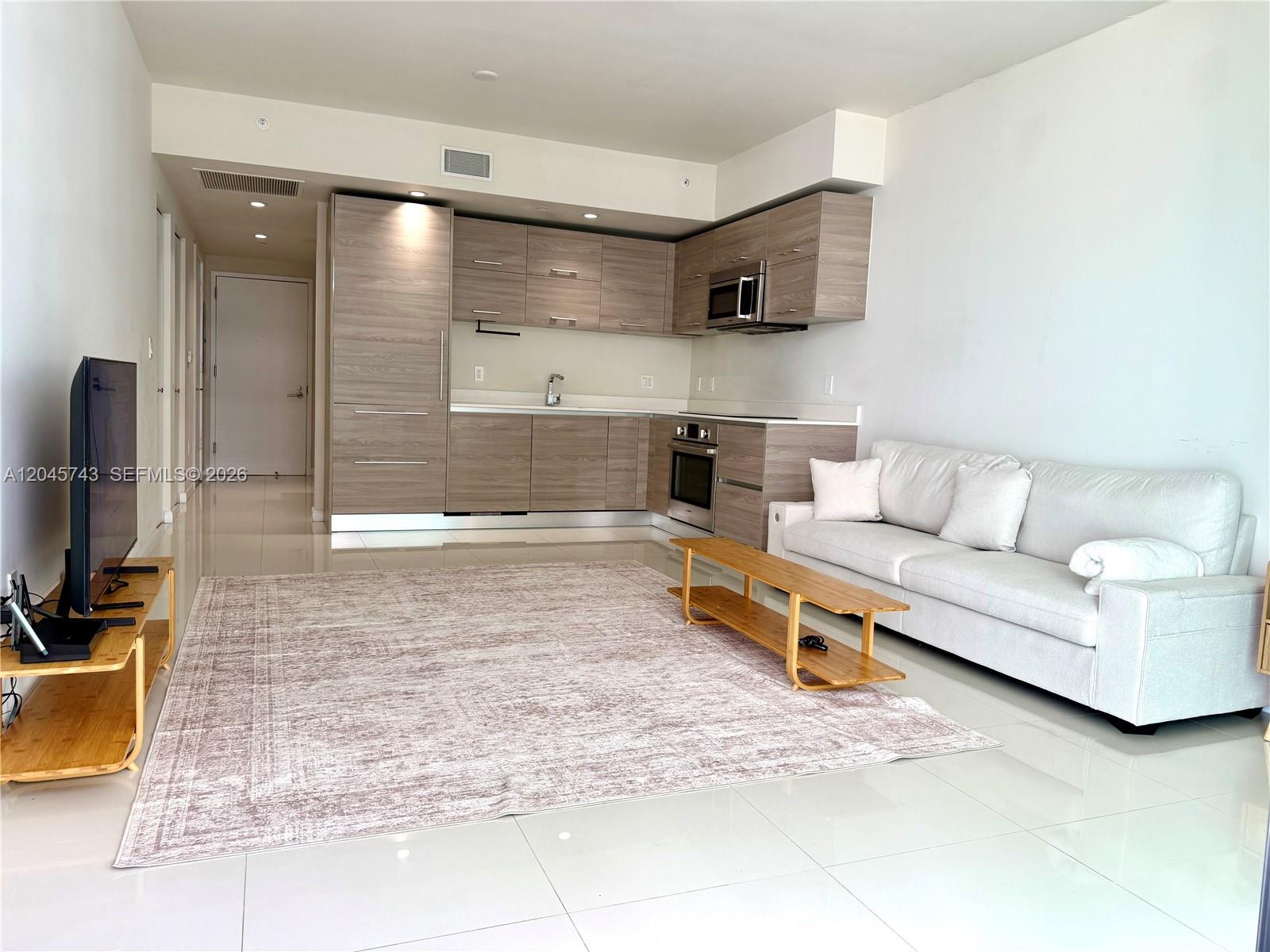 A modern open-concept living room features a kitchen with wood-grain cabinets and a white sofa — 1300 S Miami Ave # 4108, Miami FL 33130, MIAMI, FL
