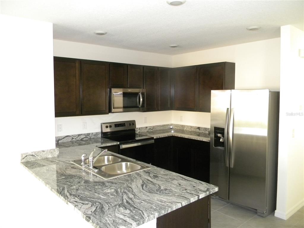 A kitchen features dark wood cabinets, granite countertops, and stainless steel appliances — 34274 JASPER STONE DRIVE, WESLEY CHAPEL, FL
