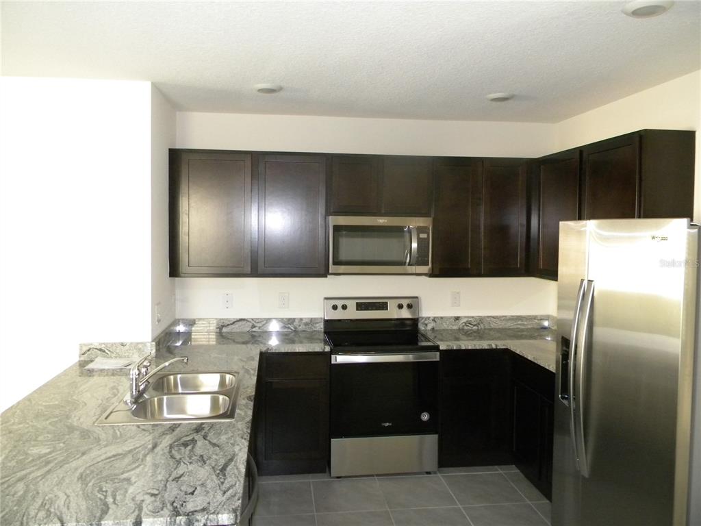 A kitchen features dark wood cabinets, granite countertops, stainless steel appliances, and gray tile flooring — 34274 JASPER STONE DRIVE, WESLEY CHAPEL, FL