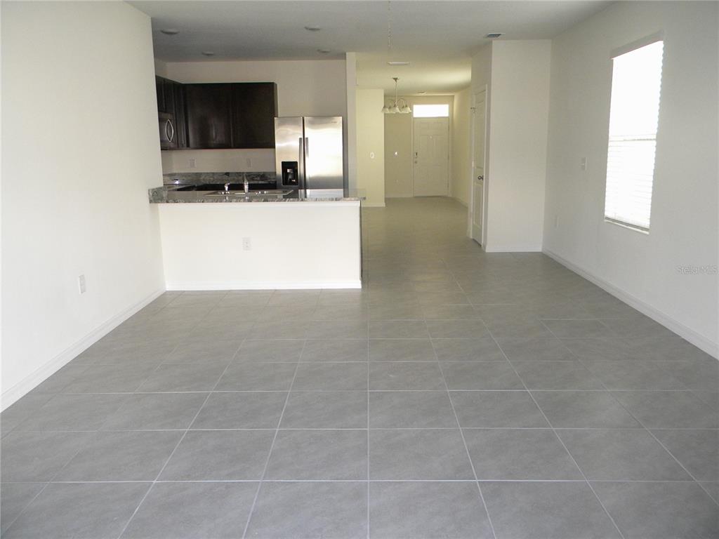 An open-concept kitchen with dark cabinets and stainless steel appliances overlooks a tiled living area — 34274 JASPER STONE DRIVE, WESLEY CHAPEL, FL