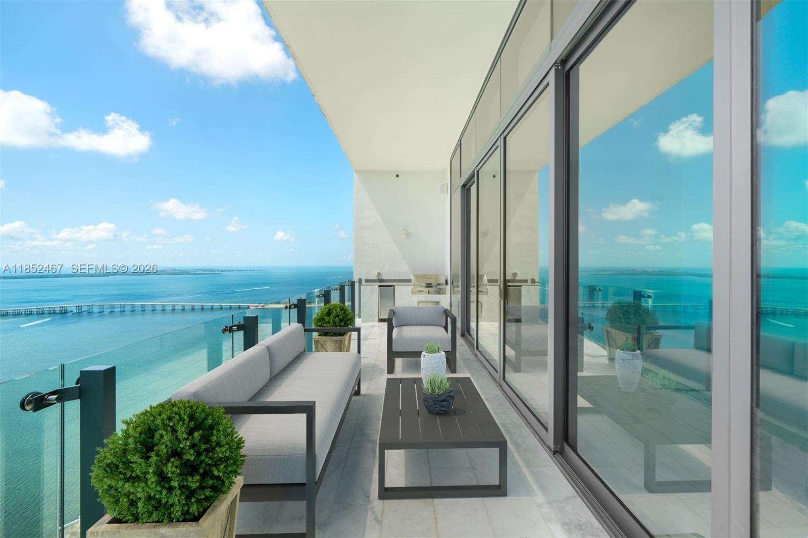 A modern balcony features outdoor furniture, glass railings, and a panoramic view of the ocean — 1451 Brickell Ave # 5302, Miami FL 33131, MIAMI, FL