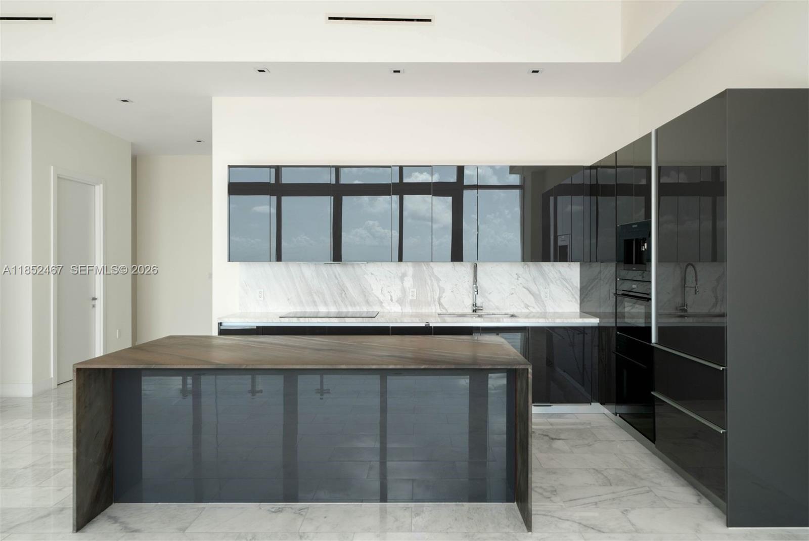 A modern kitchen features dark glossy cabinetry, a marble backsplash, and a large wood-topped island — 1451 Brickell Ave # 5302, Miami FL 33131, MIAMI, FL