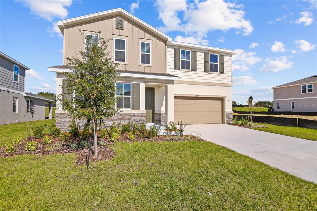 A two-story suburban house features a tan garage, stone accents, and a front yard — 1257 DAISY HILL AVENUE, DUNDEE, FL