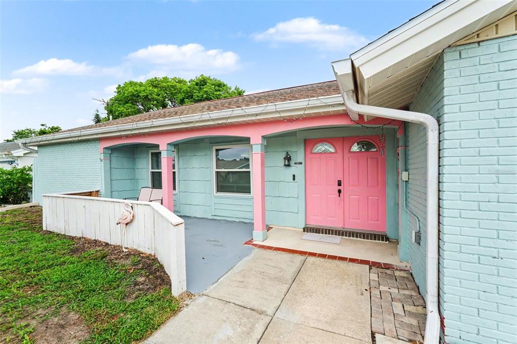 A light blue brick house features a covered porch with pink accents and pink double doors — 4315 STRATFIELD DRIVE, NEW PORT RICHEY, FL