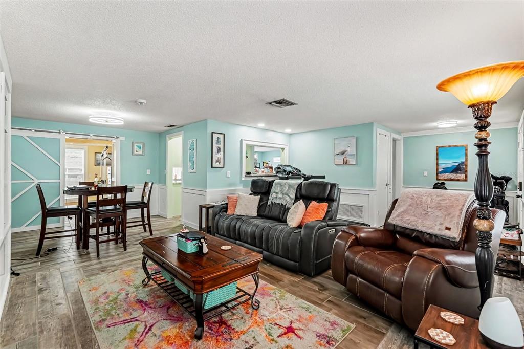 A living room with light blue walls, wood-look tile flooring, a dark sofa, and a recliner — 4315 STRATFIELD DRIVE, NEW PORT RICHEY, FL
