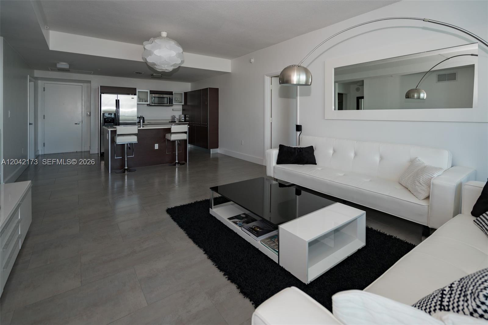 A modern living room features white leather sofas, a black coffee table, and a kitchen — MIAMI, FL