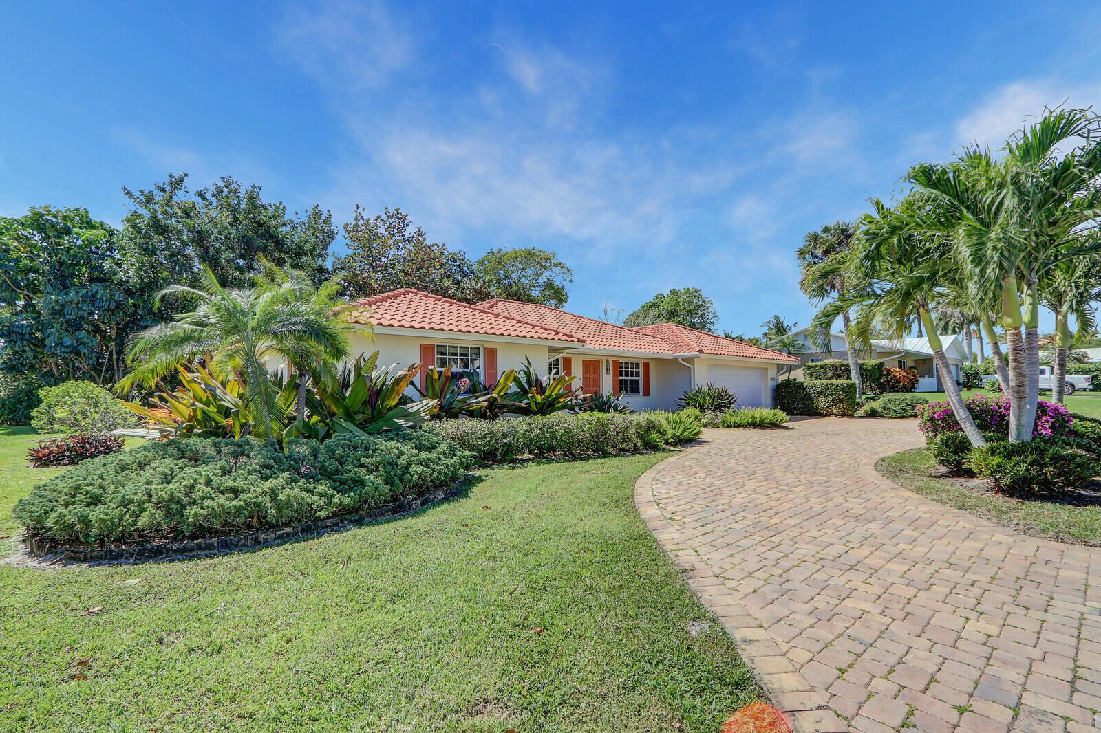 A single-story house with a red tile roof, brick driveway, and lush tropical landscaping — 8574 SE Seagrape Way, Hobe Sound FL 33455, HOBE SOUND, FL