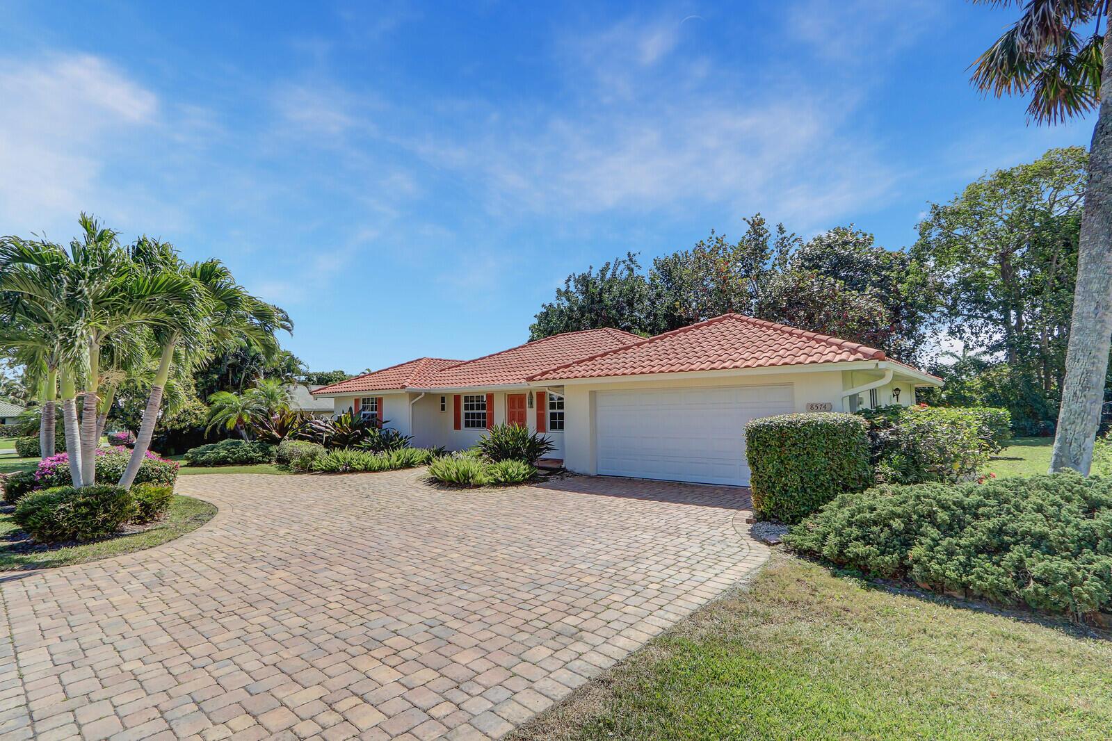 A single-story house with a terracotta tile roof and a paved driveway surrounded by landscaping — 8574 SE Seagrape Way, Hobe Sound FL 33455, HOBE SOUND, FL