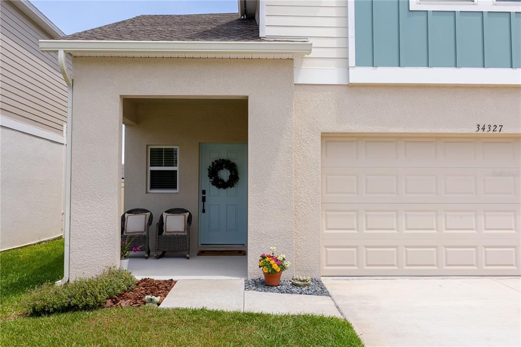 A light-colored house exterior features a covered porch, a blue front door, and a garage — 34327 VERBENA STREET, WESLEY CHAPEL, FL