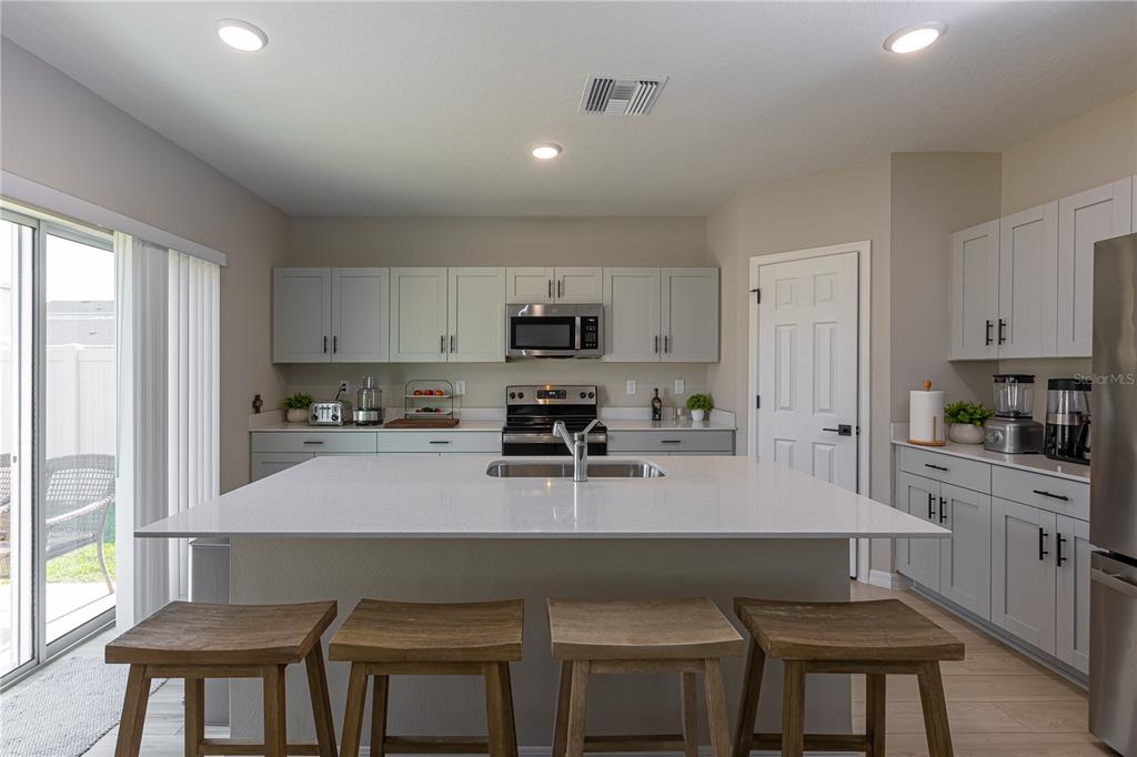 A kitchen features light gray cabinets, a white quartz island with seating, and stainless appliances — 34327 VERBENA STREET, WESLEY CHAPEL, FL