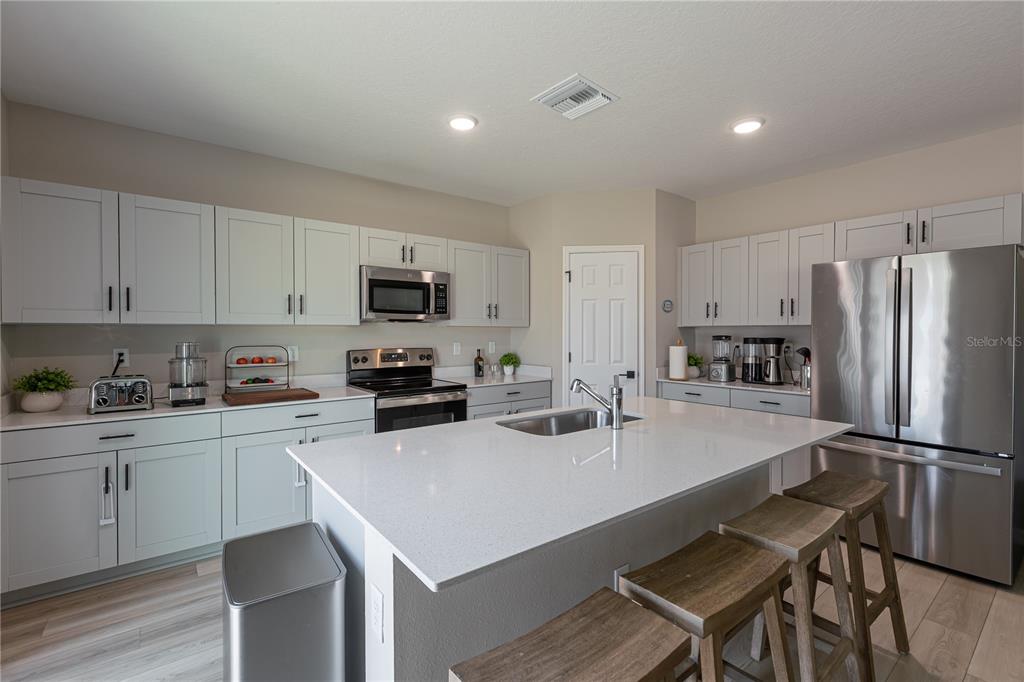A modern kitchen features light gray cabinets, white countertops, a central island, and stainless steel appliances — 34327 VERBENA STREET, WESLEY CHAPEL, FL