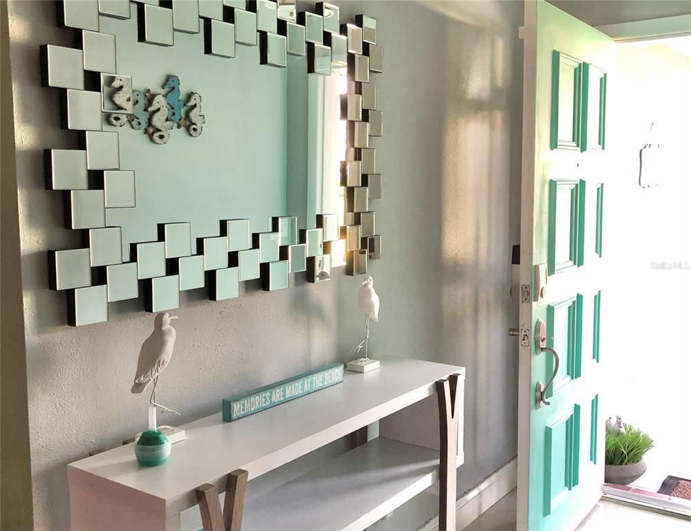 An entryway features a white console table, a decorative mirror, and a light blue door — 1237 LOTUS PATH, CLEARWATER, FL