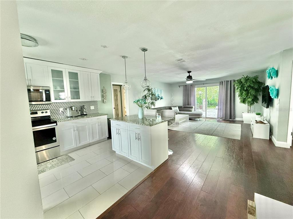 An open-concept kitchen with white cabinetry and a center island flows into a living area — 1237 LOTUS PATH, CLEARWATER, FL