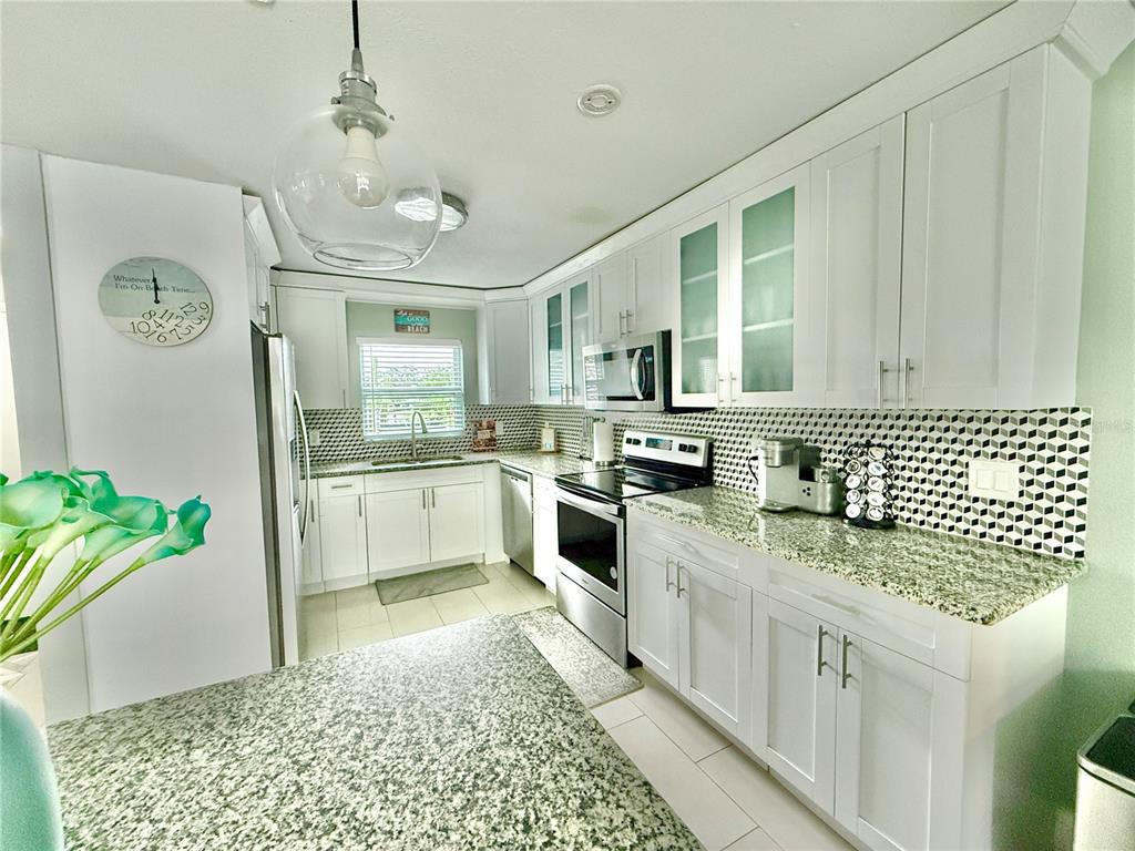A kitchen features white cabinetry, granite countertops, a geometric backsplash, and stainless steel appliances — 1237 LOTUS PATH, CLEARWATER, FL