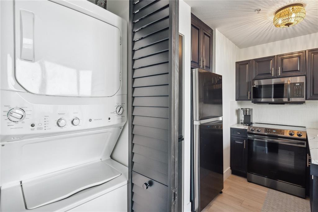 A kitchen featuring dark cabinets, stainless steel appliances, and an adjacent stacked laundry unit — 8800 BAY PINES BOULEVARD UNIT 102, ST PETERSBURG, FL