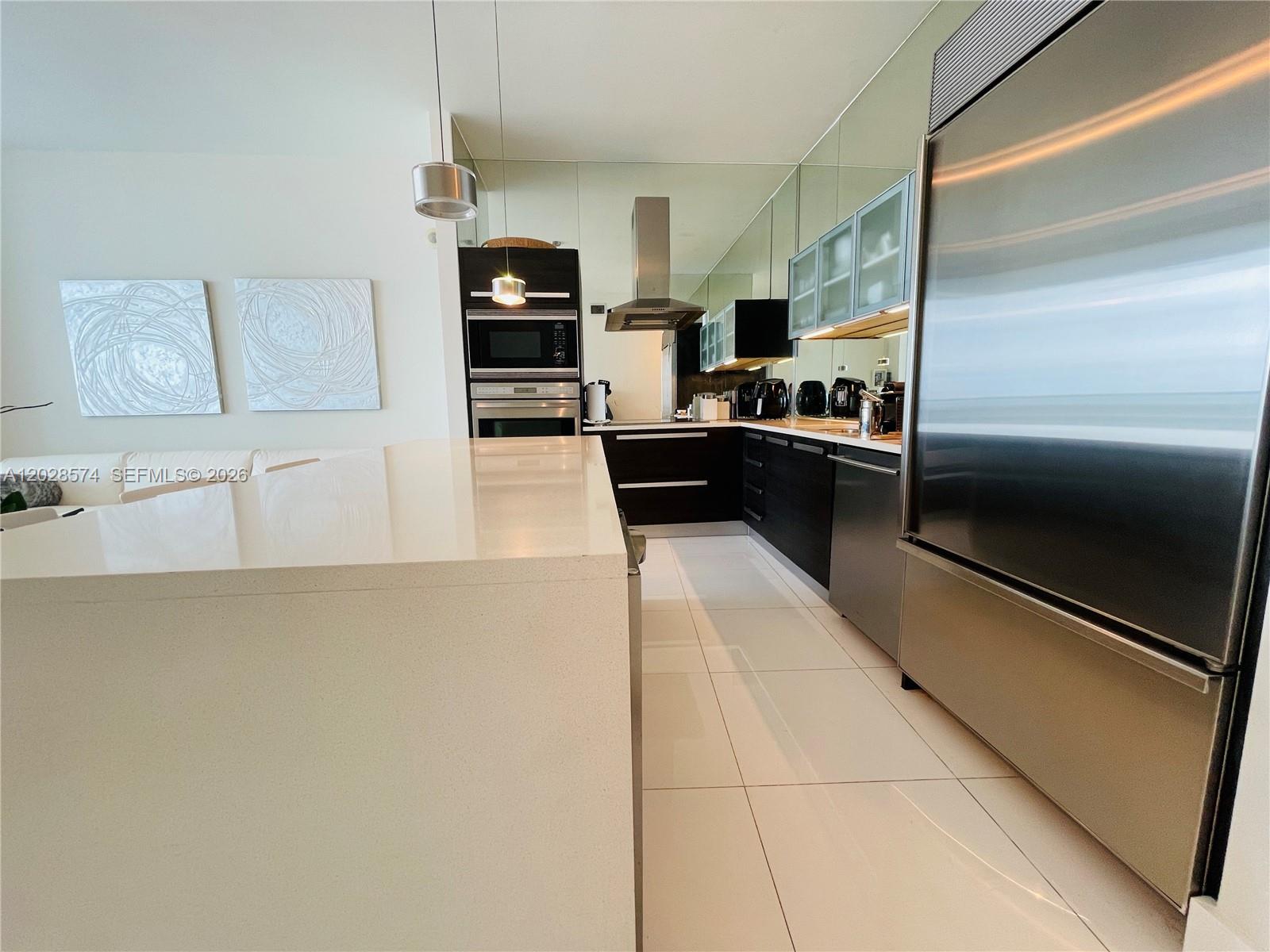 A modern kitchen features a white island, dark cabinetry, stainless steel appliances, and mirrored walls — 2020 N Bayshore Dr # 2008, Miami FL 33137, MIAMI, FL