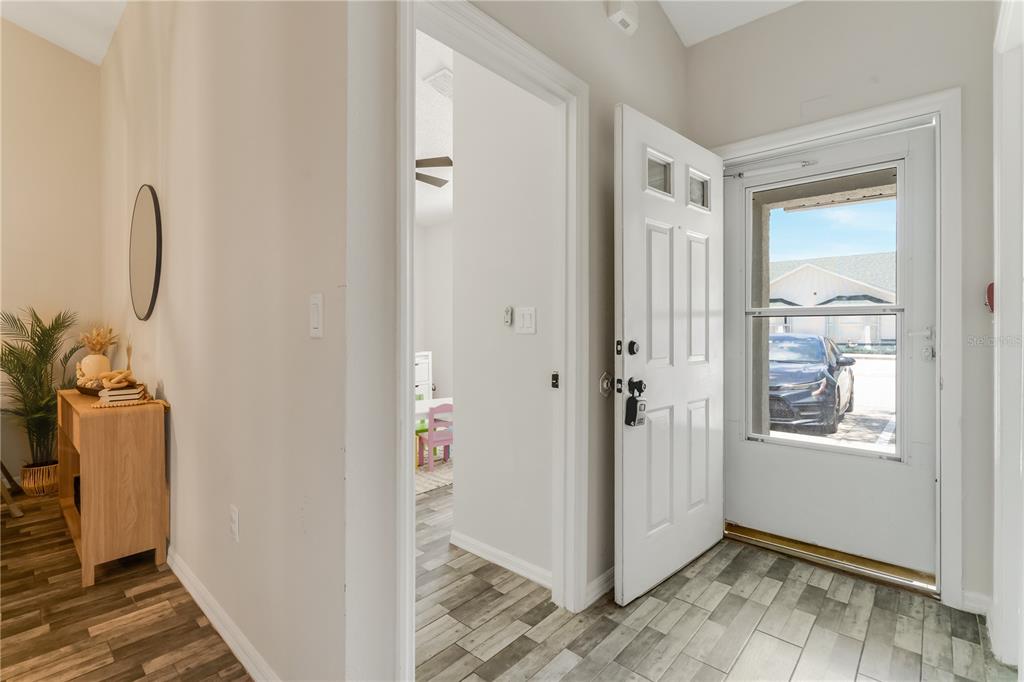 An entryway with wood-look tile flooring, a white front door, and a view into another room — 2406 KAM COURT, KISSIMMEE, FL