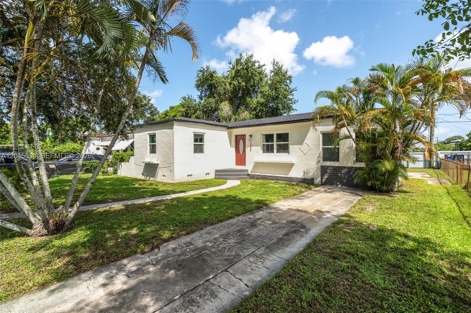 A single-story white house with a red front door, a concrete driveway, and palm trees — 1246 Fisherman St, Opa-Locka FL 33054, OPA-LOCKA, FL