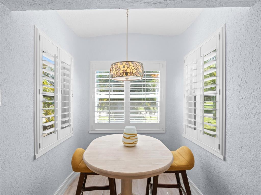 A breakfast nook features a light wood table, yellow stools, and white plantation shutters — 502 FLORIDA BOULEVARD, CRYSTAL BEACH, FL