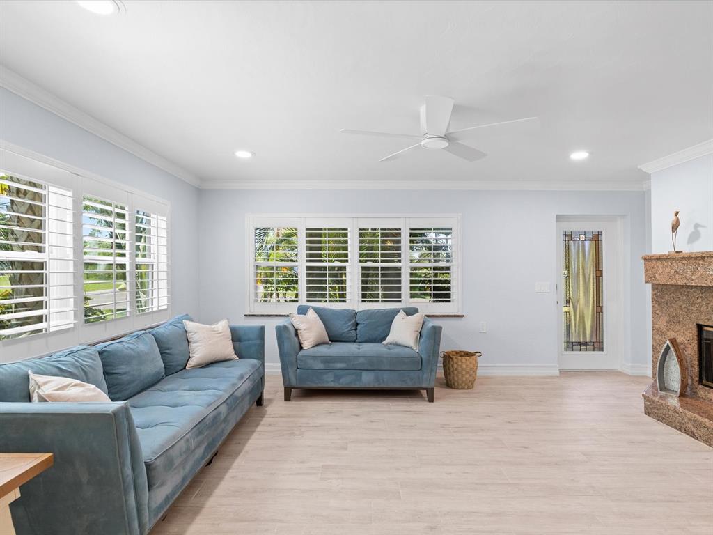 A living room features blue sofas, light wood-look flooring, plantation shutters, and a stone fireplace — 502 FLORIDA BOULEVARD, CRYSTAL BEACH, FL