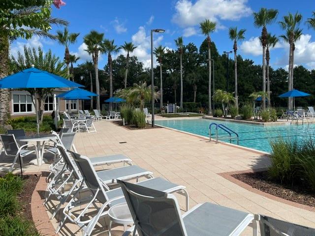 A swimming pool area features lounge chairs, blue umbrellas, and palm trees under a sunny sky — 1351 VENEZIA COURT UNIT 305, DAVENPORT, FL