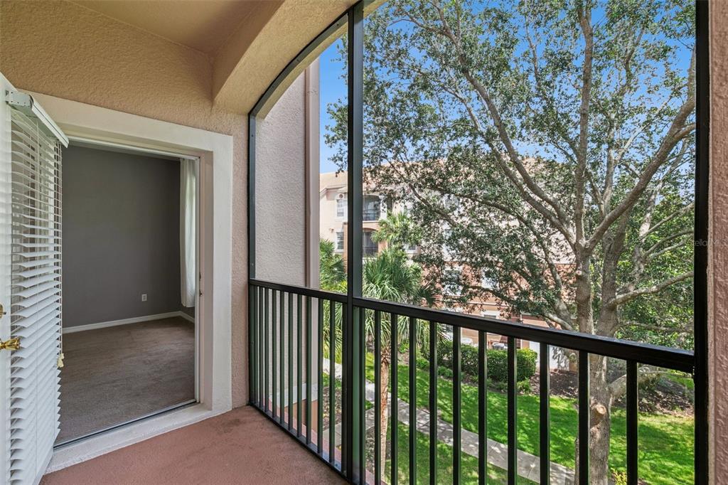 A screened-in balcony overlooks a grassy courtyard and trees outside a carpeted interior room — 1351 VENEZIA COURT UNIT 305, DAVENPORT, FL